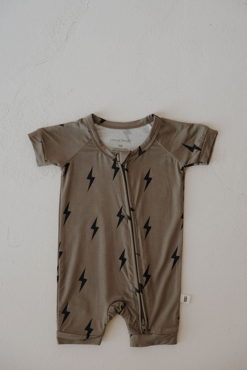 The forever french baby Bamboo Zip Shortie in Brown & Black Lightning Bolt is a short-sleeved, hypo-allergenic romper with a front zipper—perfect for those seeking breathable comfort for their little one.