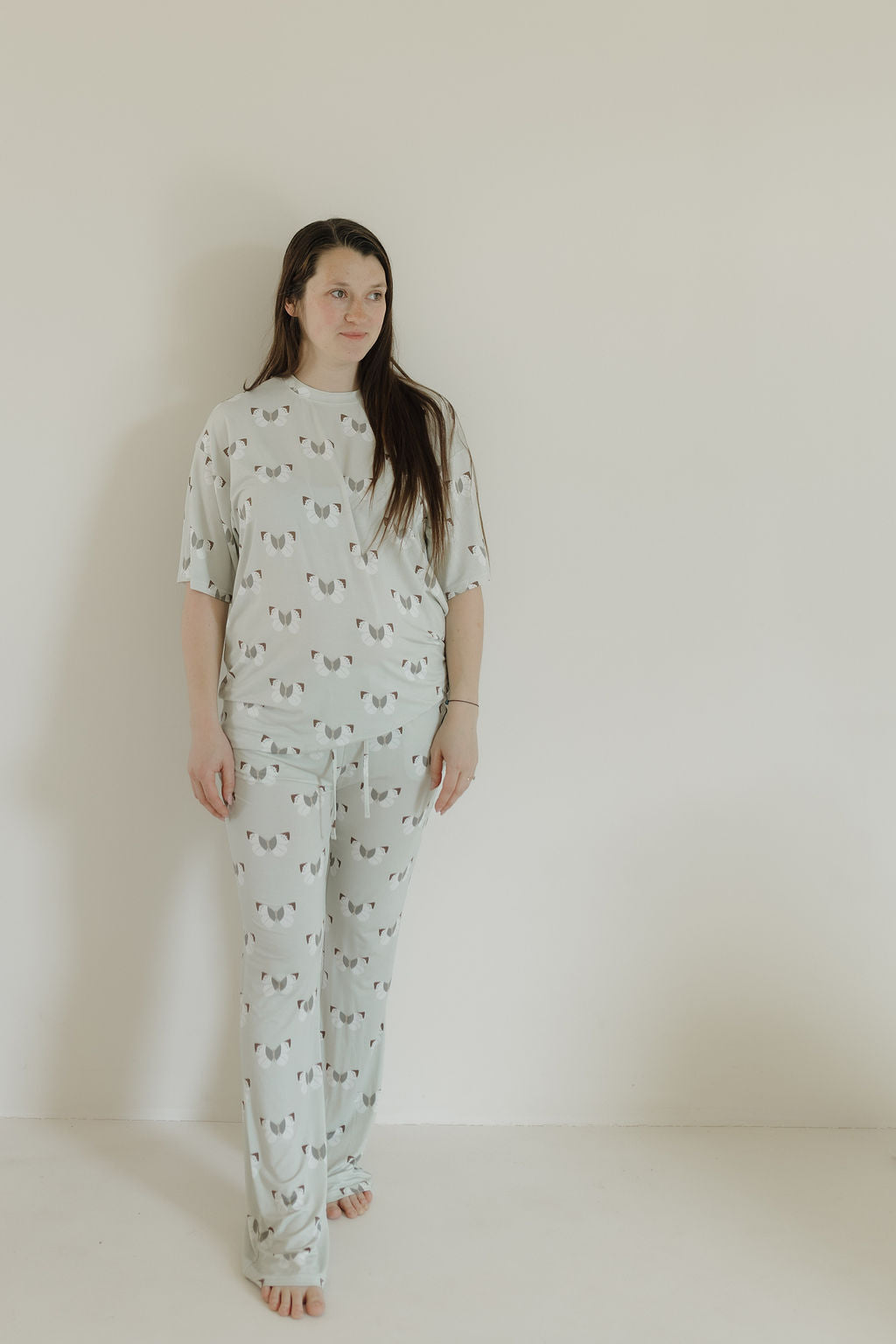 Barefoot before a plain white wall, the person wears an oversized pajama set from forever french baby. Their long hair complements their calm expression while they don cozy Short Sleeve Women's Bamboo Pajamas with a butterfly print, ensuring comfort all night.