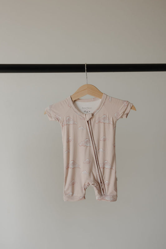 The Kendy 3 Bamboo Zip Shortie | Ruby, a light pink, short-sleeved breathable romper, hangs on a wooden hanger against a plain light background.