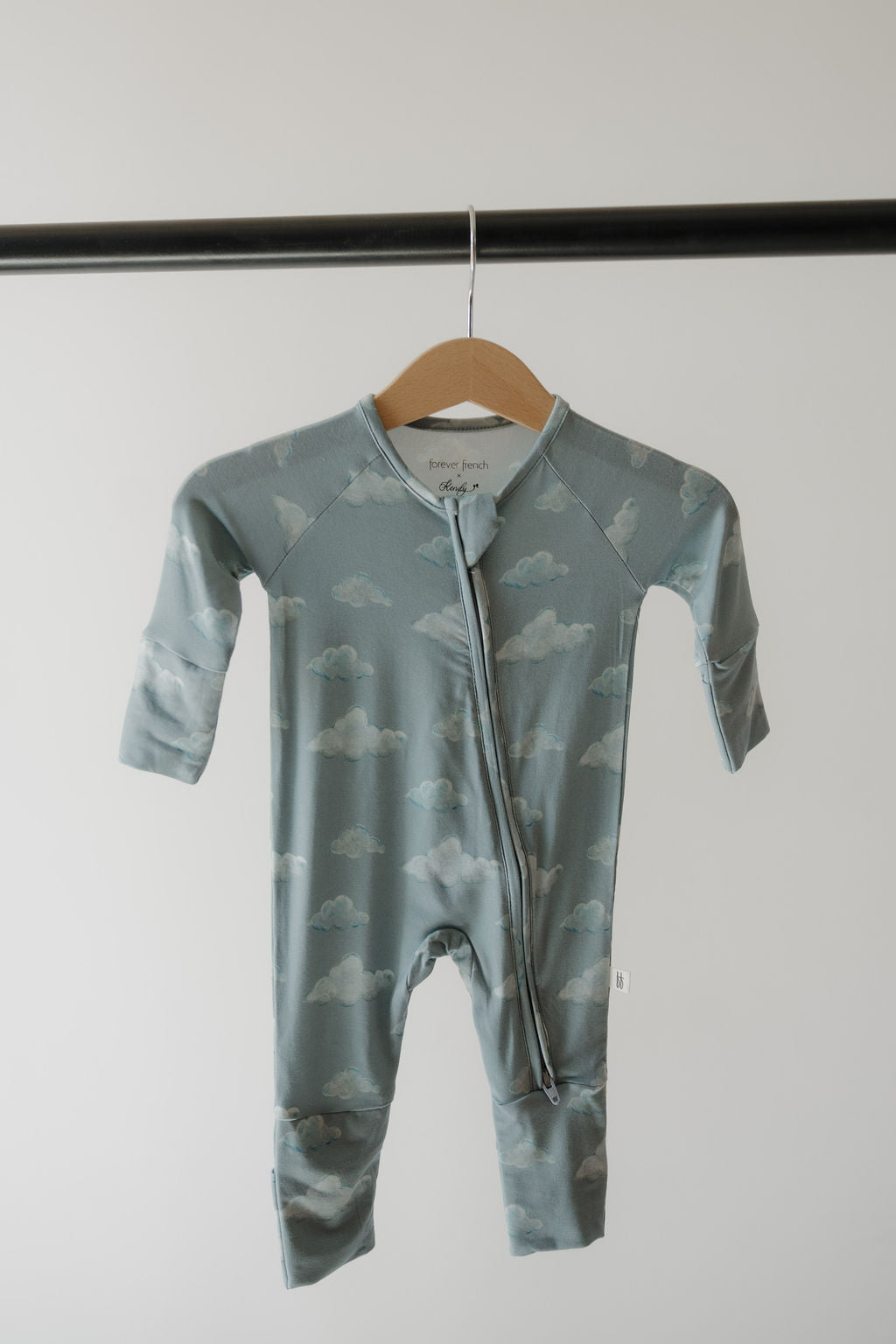 The Bamboo Zip Pajamas | Duke by Kendy 3, in blue-green with a cloud pattern and made from breathable fabric, hangs on a wooden hanger from a black rod against a plain light background.