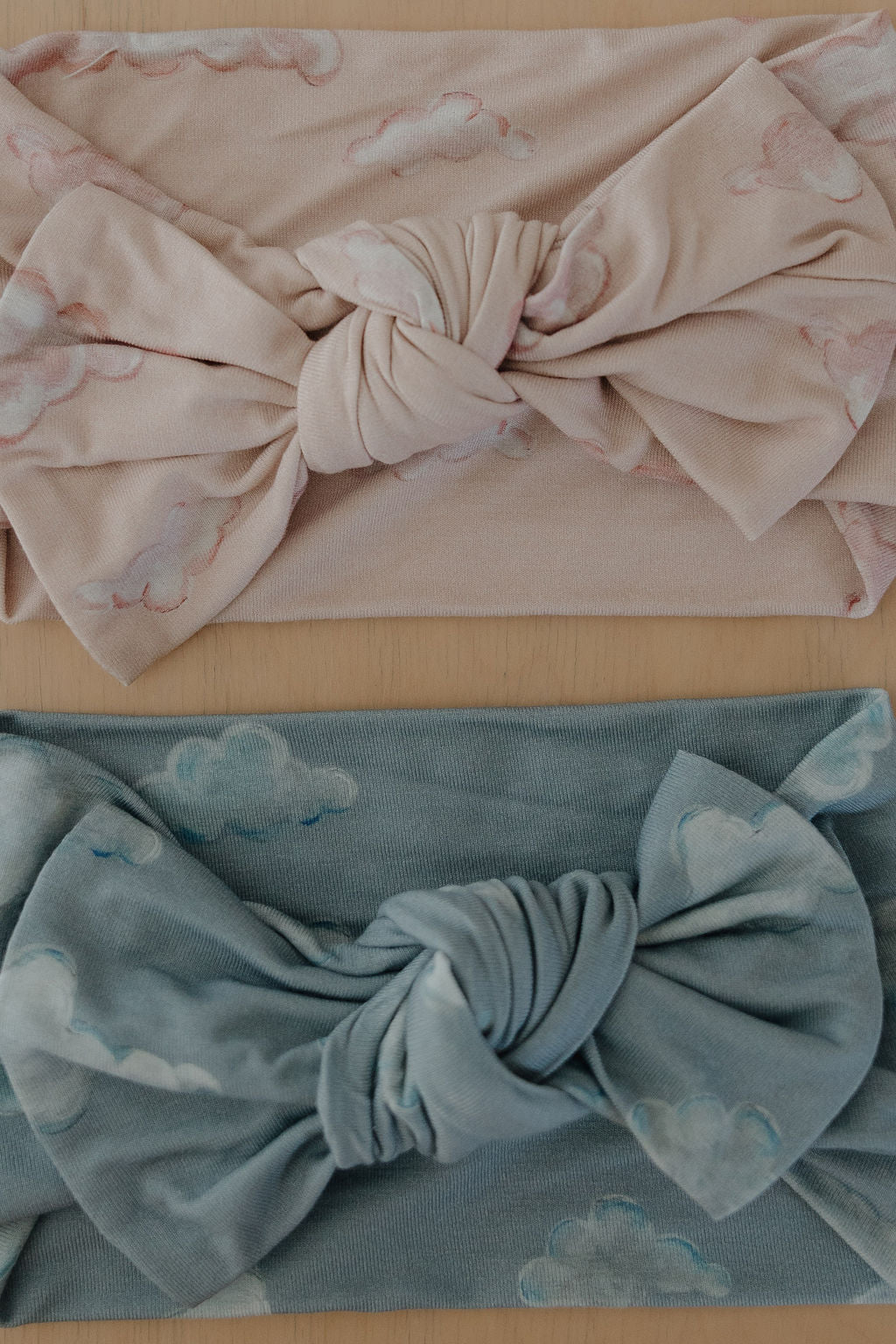 Two Kendy 3 Bamboo Head Wraps | ff x kendy, each with a large knotted bow, are displayed on wood: the top one is light pink with a cloud pattern; the bottom is light blue with white clouds.