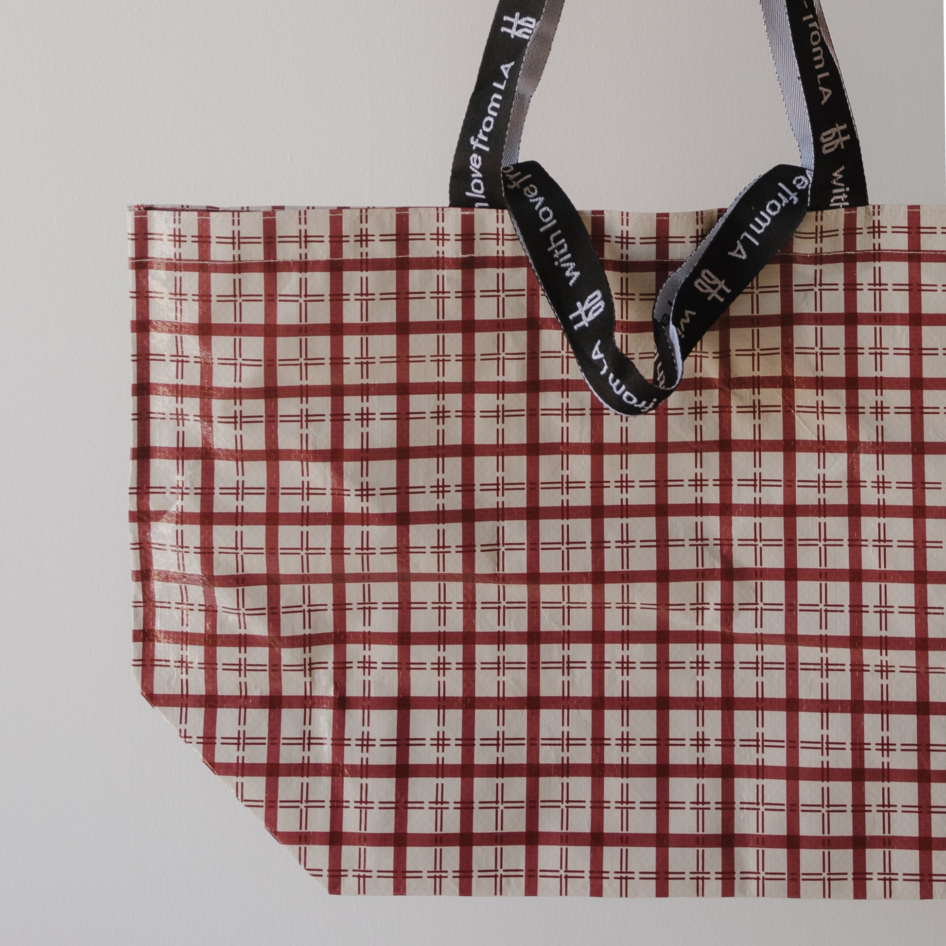 The ff Tote Bag | Window Pane by forever french baby hangs on a wall. This large rectangular tote features a red and white checkered pattern, black handles with "With love from LA" in white, and is made from durable woven polypropylene.