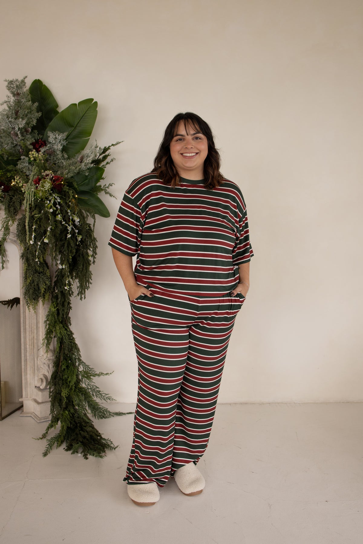 A person wears the forever french baby Women’s Boxy Tee Lounge Set in Holiday Stripe, featuring a boxy short-sleeved t-shirt and matching wide-leg lounge pants in a red, green, and white horizontal stripe pattern.
