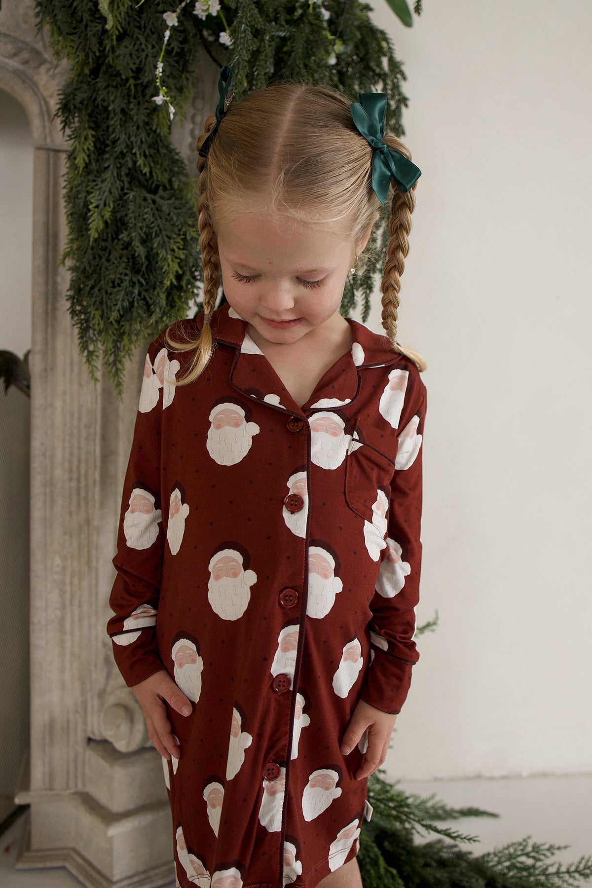 A young child wearing a long-sleeved Bamboo Sleeping Dress | Vintage Santa featuring a repeating pattern of vintage Santa Claus faces.