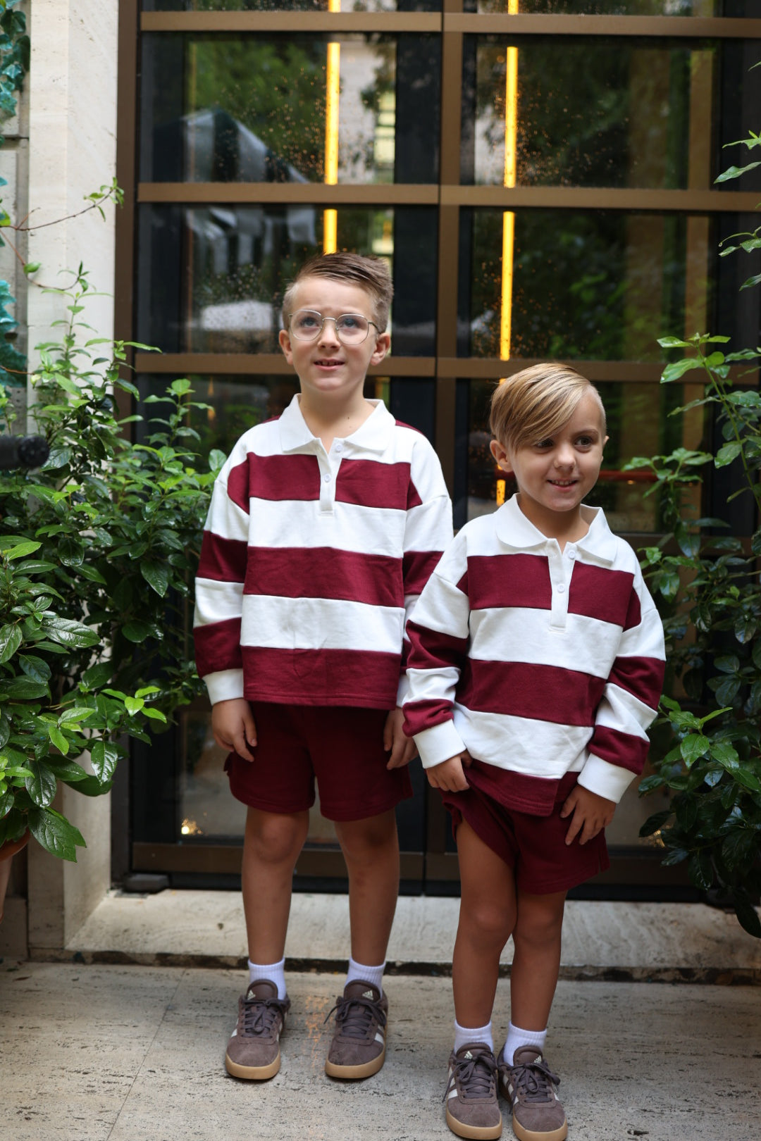 Two boys stand side by side wearing matching white and deep red Child Rugby Sweatshirt | Deep Cranberry tops and coordinating shorts.