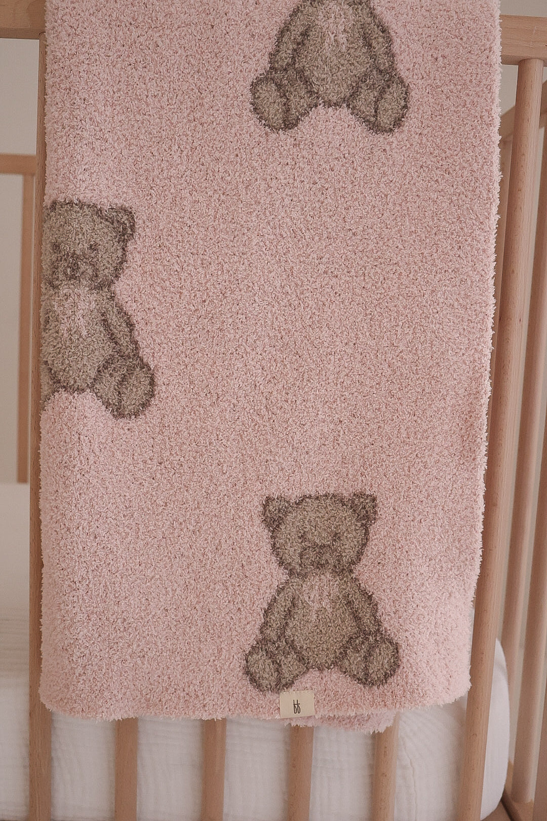 The forever french baby Plush Blanket | Lottie, Oeko-Tex certified for safety and comfort, features soft pink microfiber and light brown teddy bear designs, shown draped over a wooden crib.
