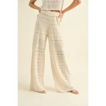 A person stands against a beige background wearing a sleeveless top and Crochet Pattern Pants by MIOU MUSE, featuring wide-leg design and intricate lace patterns that emphasize the beauty of the fabric. The person's face is not visible.