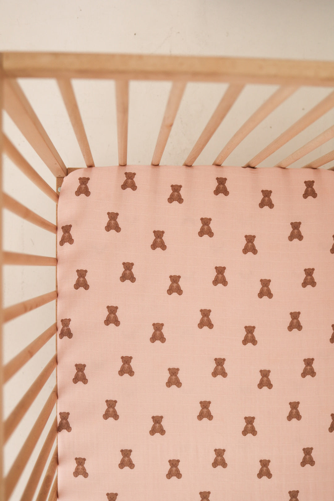 A top-down view of the forever french baby Muslin Crib Sheet | Pink Lottie, featuring a pink fabric with a playful brown teddy bear pattern—an adorable and cozy choice for your baby's crib bedding.