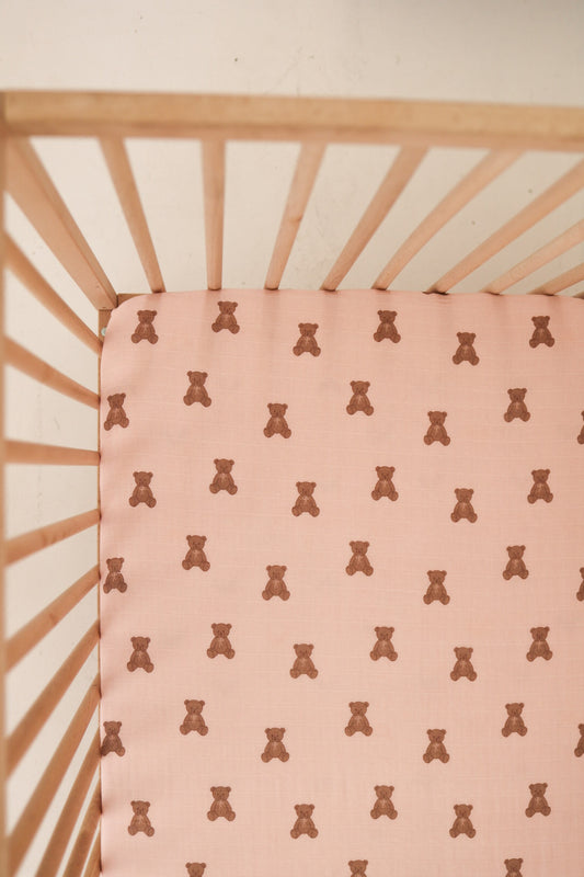 A top-down view of the forever french baby Muslin Crib Sheet | Pink Lottie, featuring a pink fabric with a playful brown teddy bear pattern—an adorable and cozy choice for your baby's crib bedding.