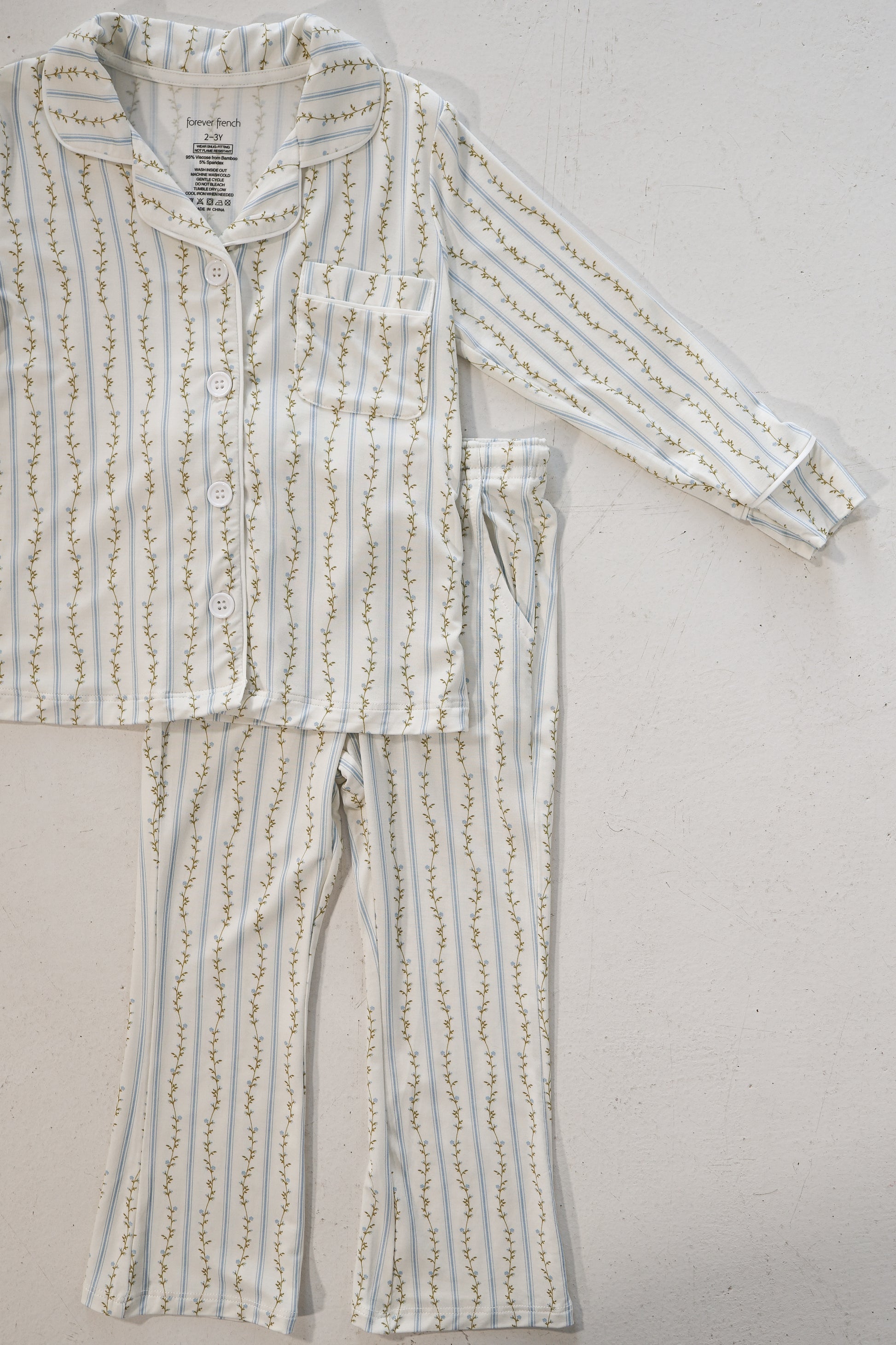 The Girl’s Bamboo Button Up Lounge Set | Dainty Vines by forever french baby is a children’s white pajama set with long sleeves and pants, made from hypo-allergenic bamboo, featuring yellow and green floral vines.