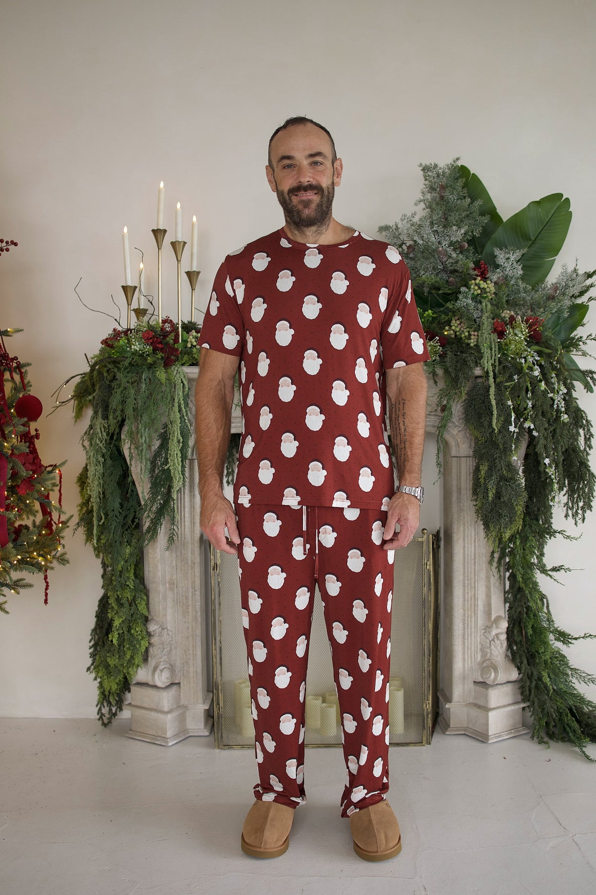 A man wearing the Men’s Short Sleeve Pajamas | Vintage Santa, a short-sleeve bamboo pajama set with matching pants featuring a repeating pattern of Santa Claus faces.