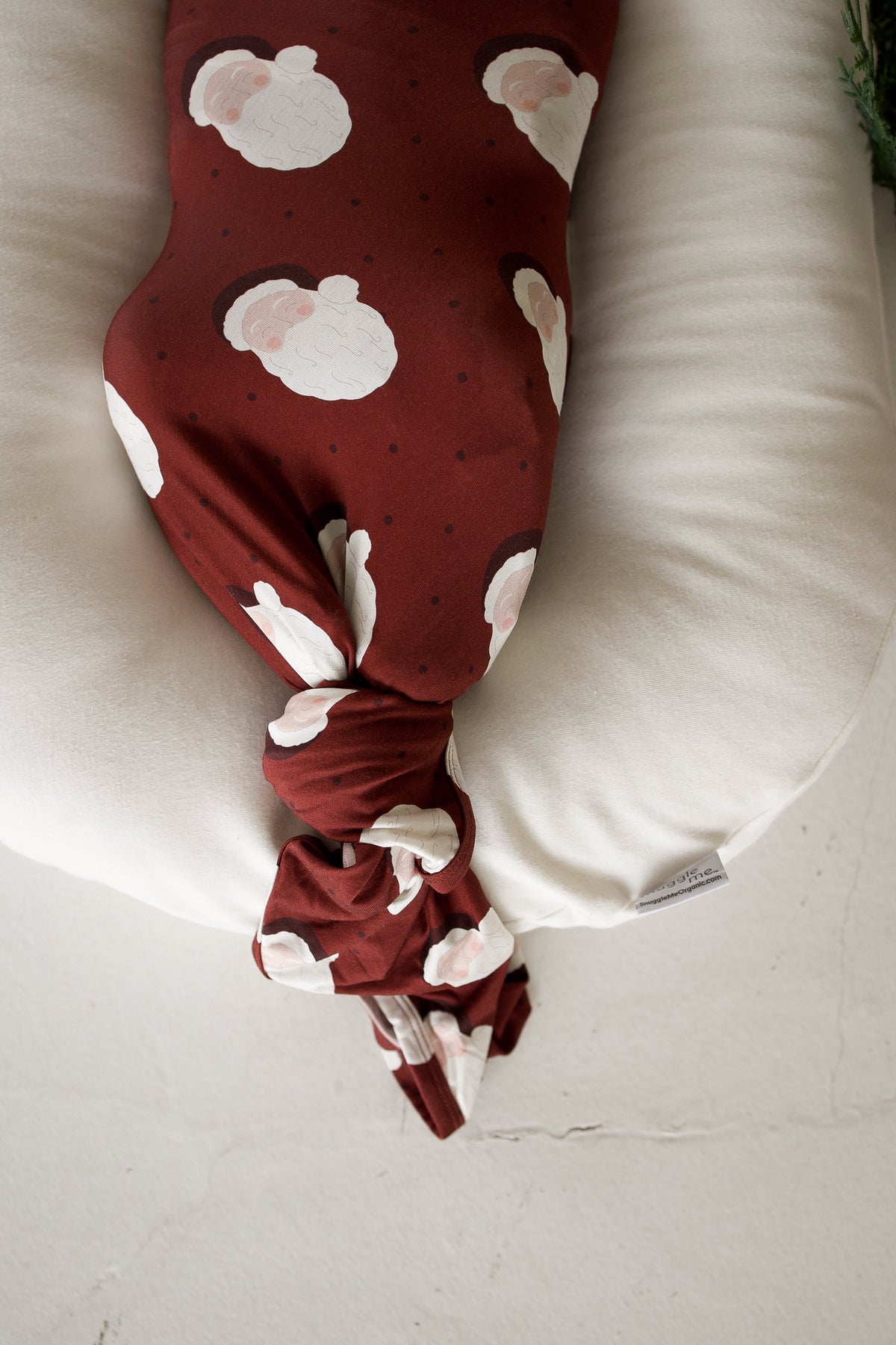 An infant wrapped in a Bamboo Swaddle | Vintage Santa, lying in a cream-colored baby lounger.