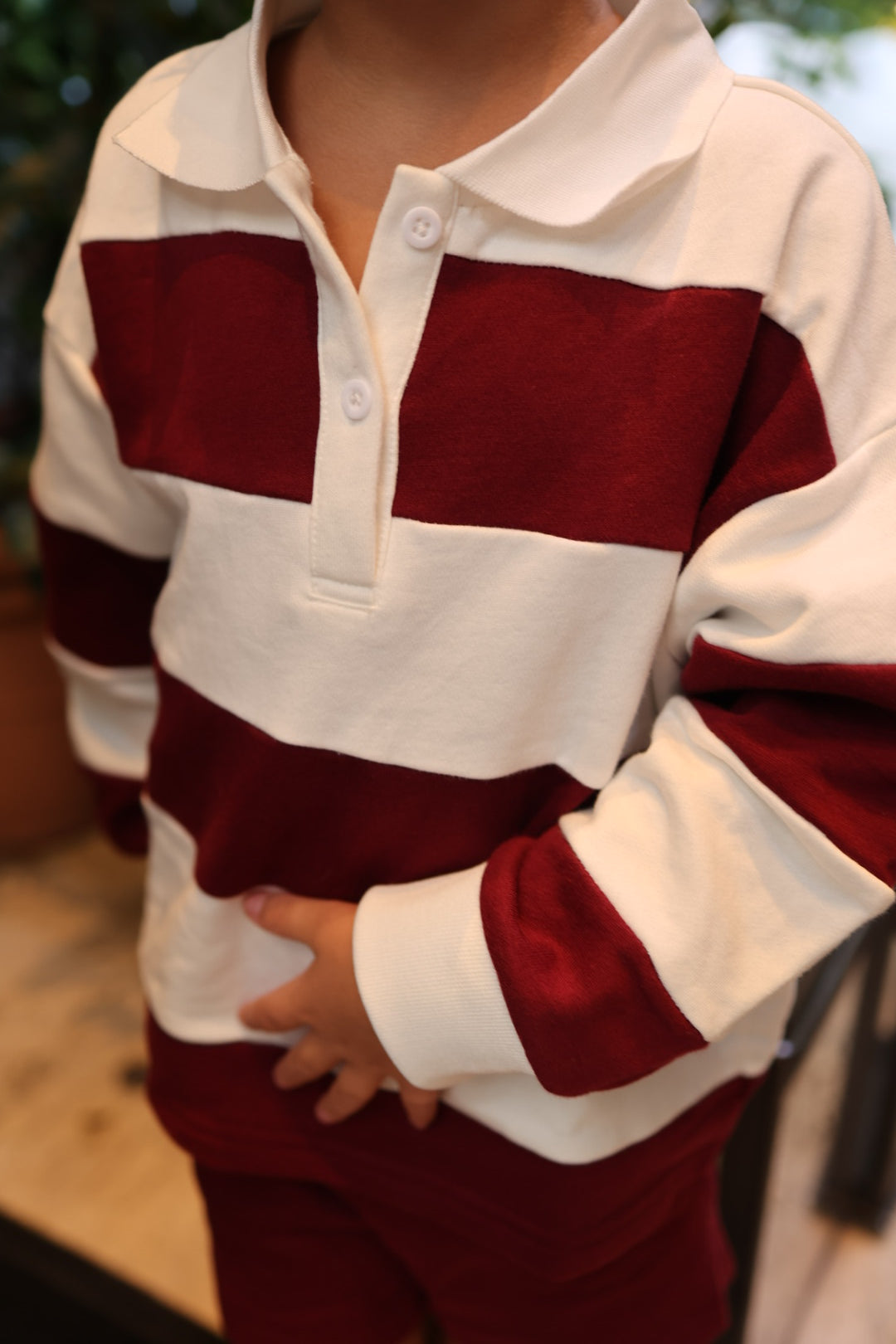 A child wearing a Child Rugby Sweatshirt | Deep Cranberry, featuring a long-sleeved, 100% cotton design with thick, horizontal burgundy and white stripes.