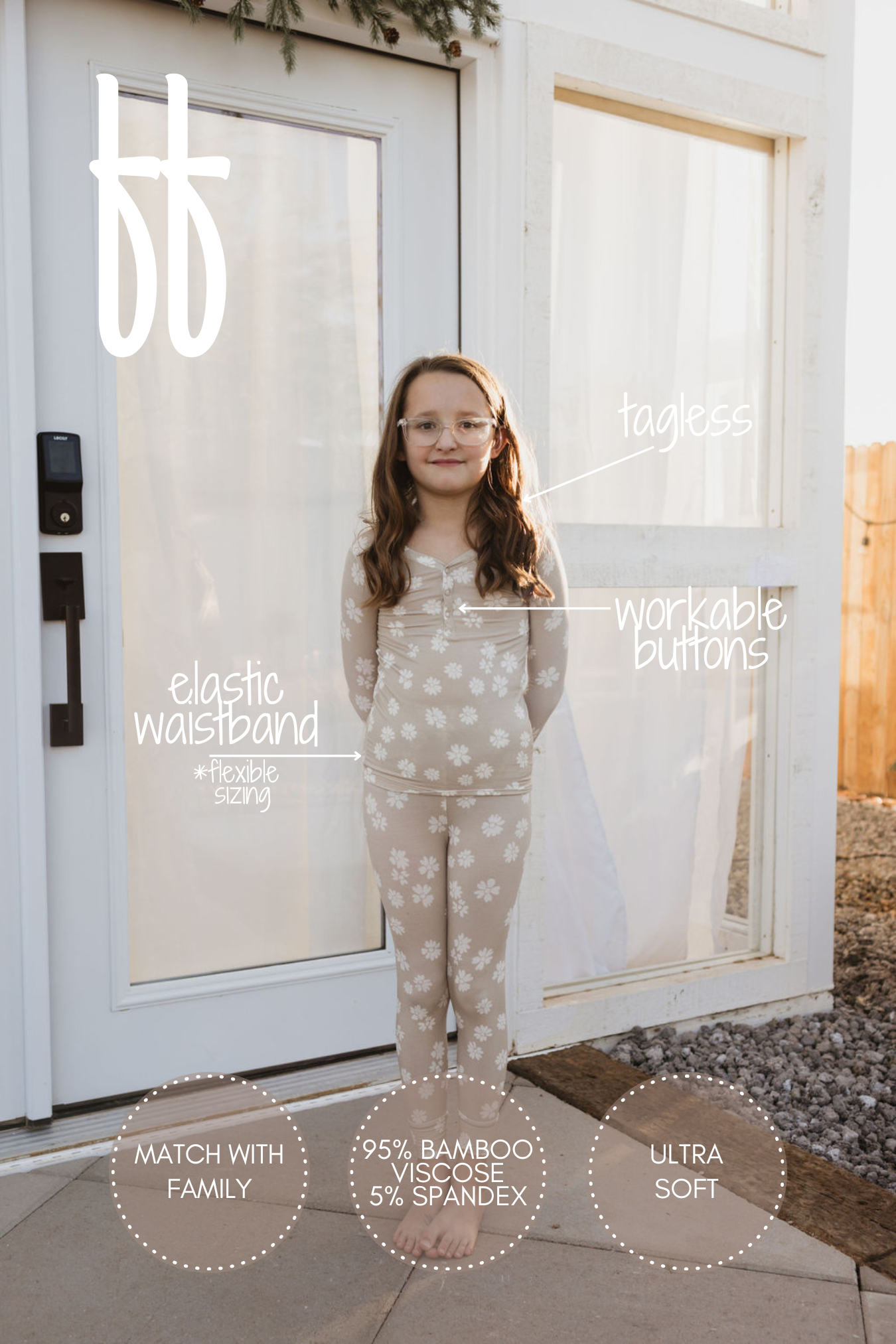 A young girl smiles while wearing the Lazy Daisy bamboo two-piece pajamas from forever french baby, showcasing a delightful pattern. These hypo-allergenic pajamas feature an elastic waistband, a tagless design, and functional buttons, crafted from 95% bamboo viscose and 5% spandex. She stands outdoors in front of a white building.