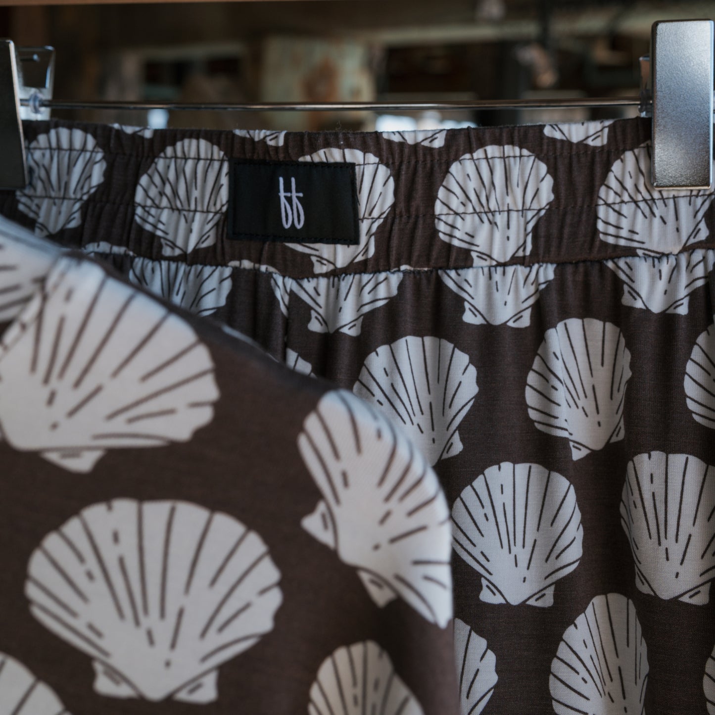 The forever french baby Child Boxy Tee Lounge Set | Seashells, made from breathable, hypo-allergenic bamboo, features a white seashell pattern on brown fabric with a black waistband label. Another matching piece is visible in the foreground.