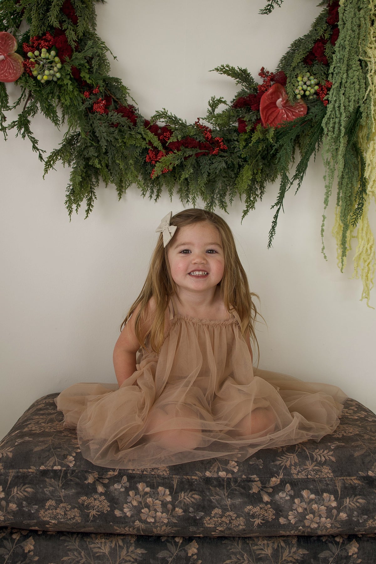 A young girl sits on a patterned cushion wearing a forever french baby Tutu Dress | Teddy in tan tulle with bow straps.