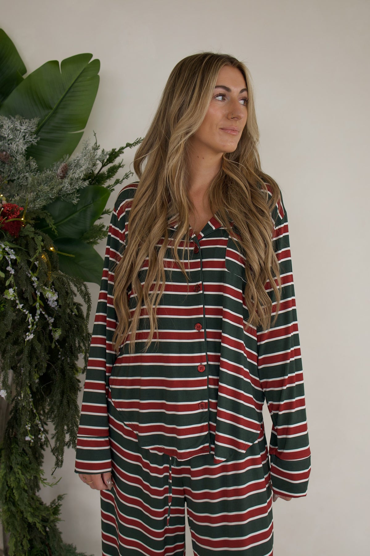 A woman wears the forever french baby Women’s Bamboo Button Up Lounge Set in Holiday Stripe, a long-sleeved button-down pajama top and matching wide leg lounge pants featuring red, green, and white horizontal stripes.