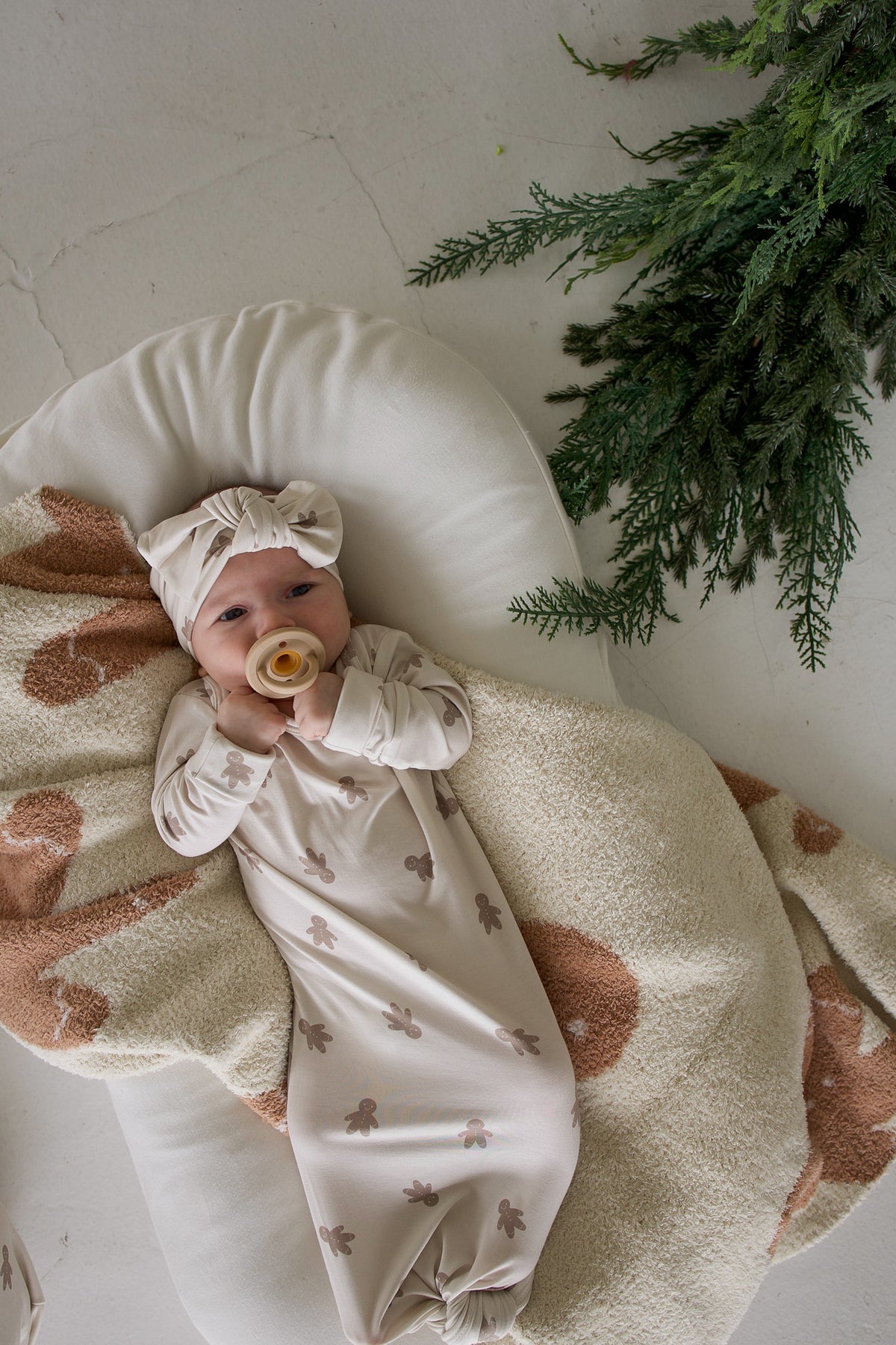 A baby wearing a Bamboo Knotted Gown | Gingersnap and matching headband, lying on a plush blanket while holding a pacifier.
