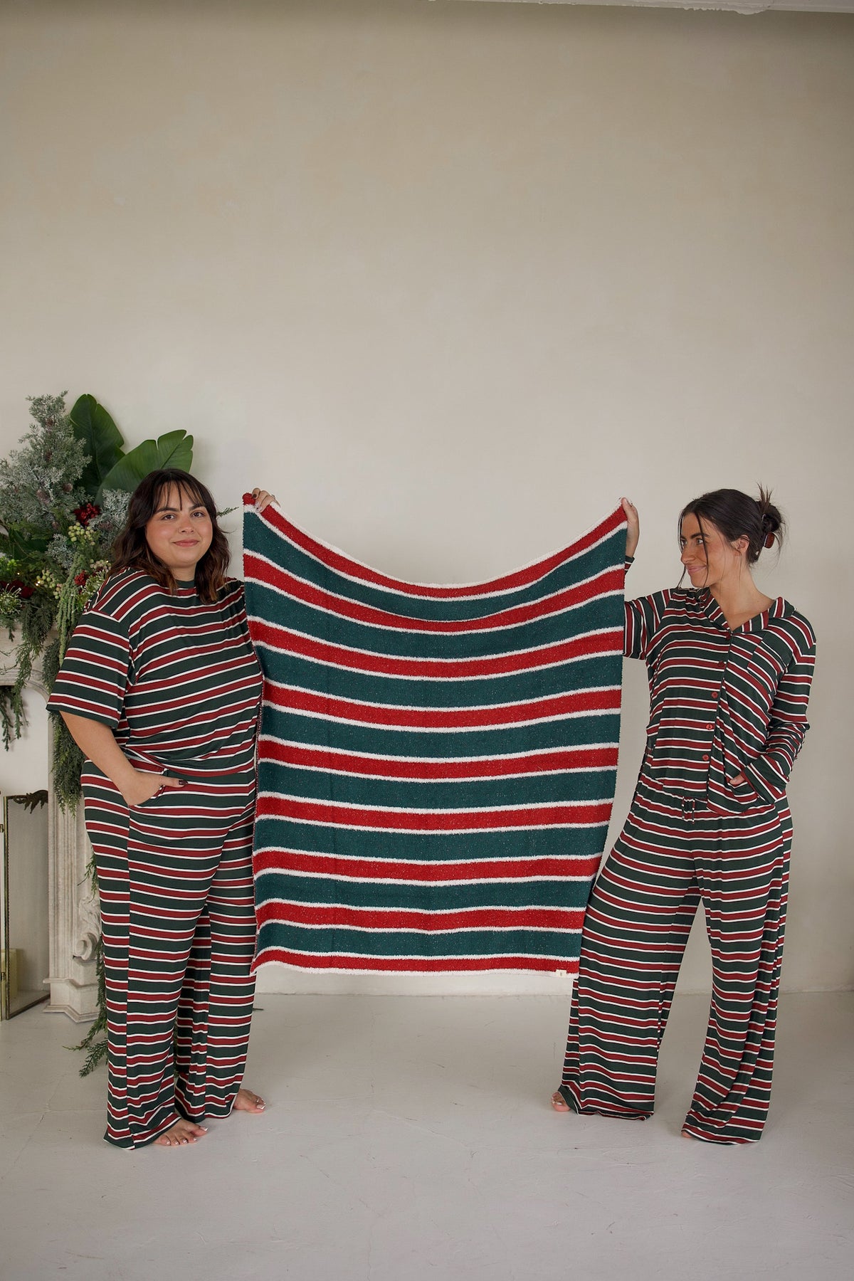 Two women in matching holiday stripe pajamas hold up a *PRE-ORDER* Plush Blanket | Holiday Stripe with horizontal red, green, and white stripes.