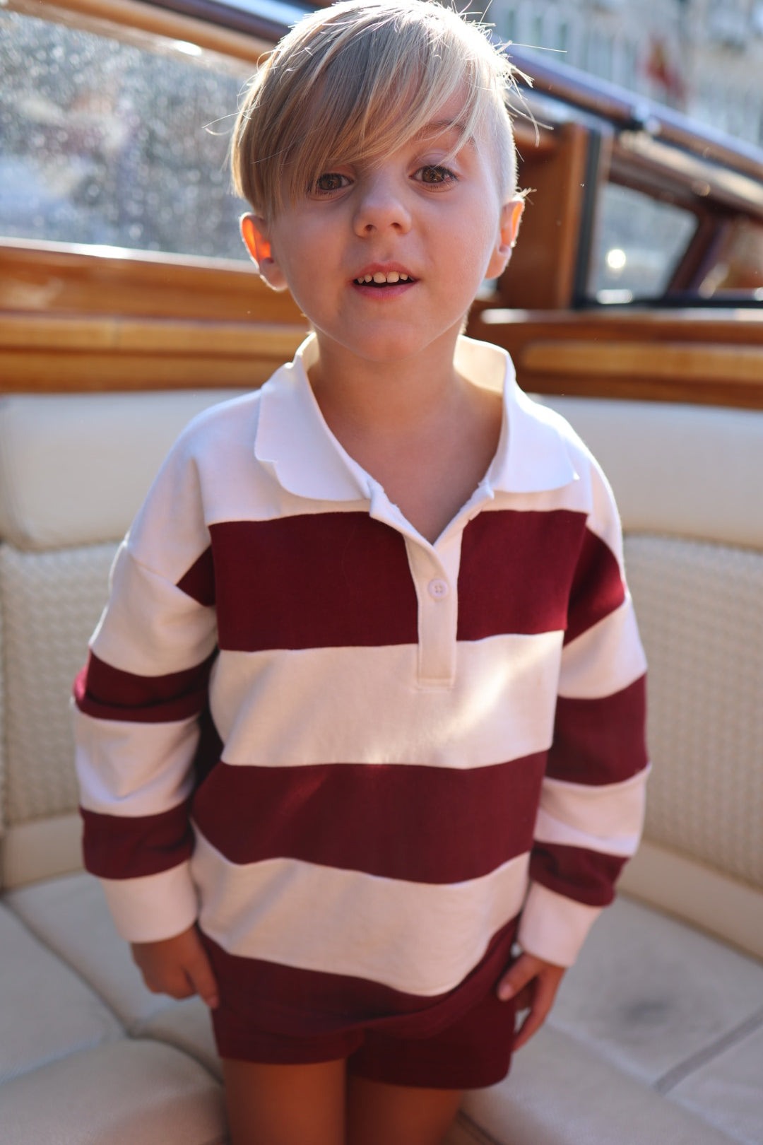 A child wearing a 100% cotton Child Rugby Sweatshirt | Deep Cranberry featuring wide, horizontal cranberry and white stripes and a white collar.