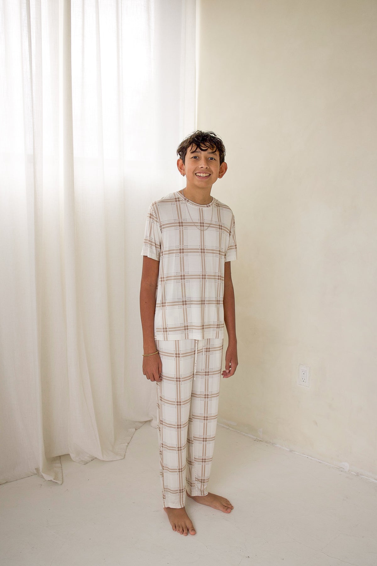 A boy wearing Youth Straight Leg Bamboo Pajamas in Ellis Plaid, featuring a tan and white short-sleeved top and matching straight-leg pants.