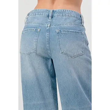 The person is wearing the High Rise Skater Jeans by I&M JEAN, INC. These jeans come in a medium wash with a light blue, slightly faded denim look. From the back, they feature two back pockets for a classic appeal.