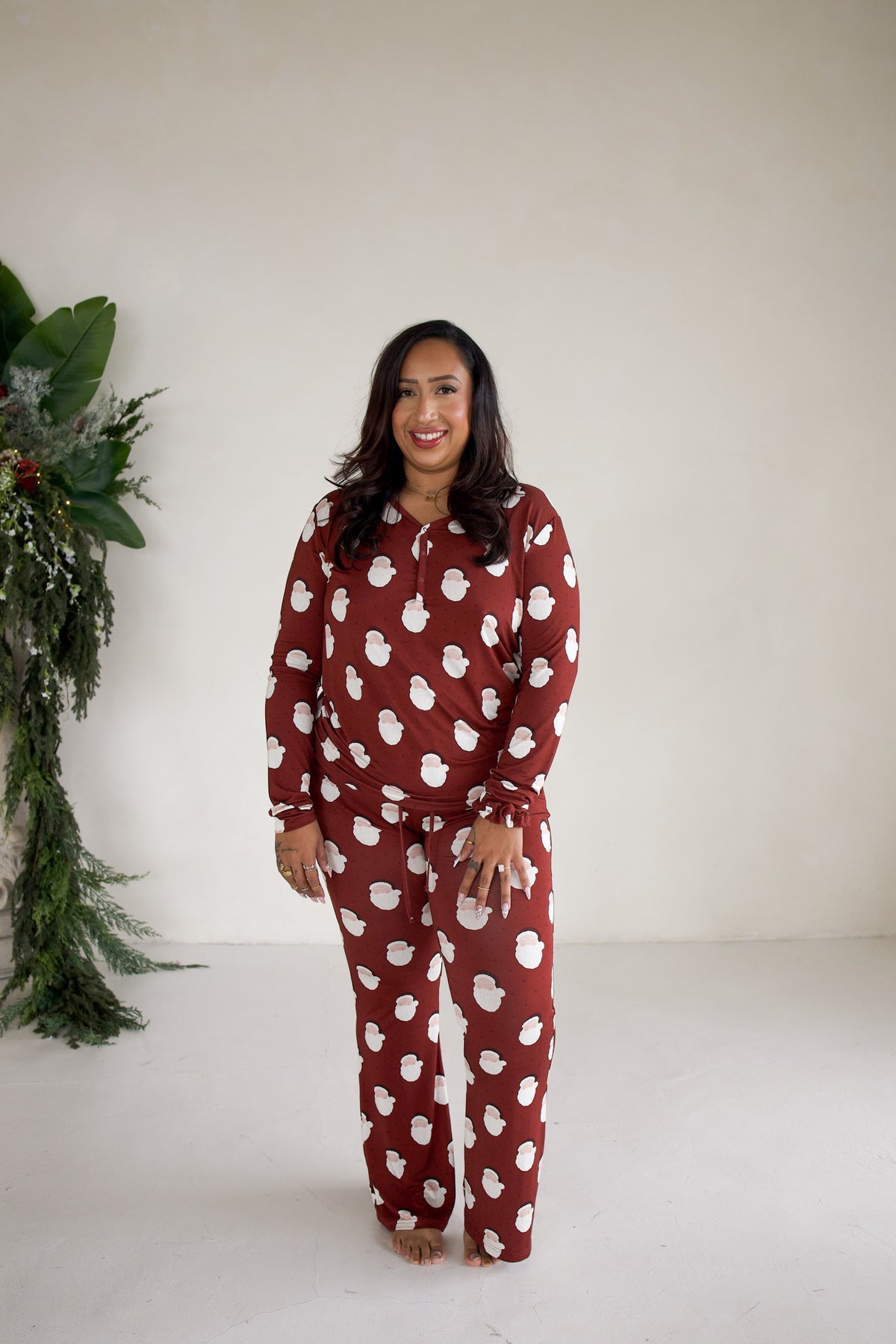 A woman wearing a dark red, long-sleeve Women’s Long Sleeve Bamboo Pajama | Vintage Santa set featuring a white Santa Claus face print.