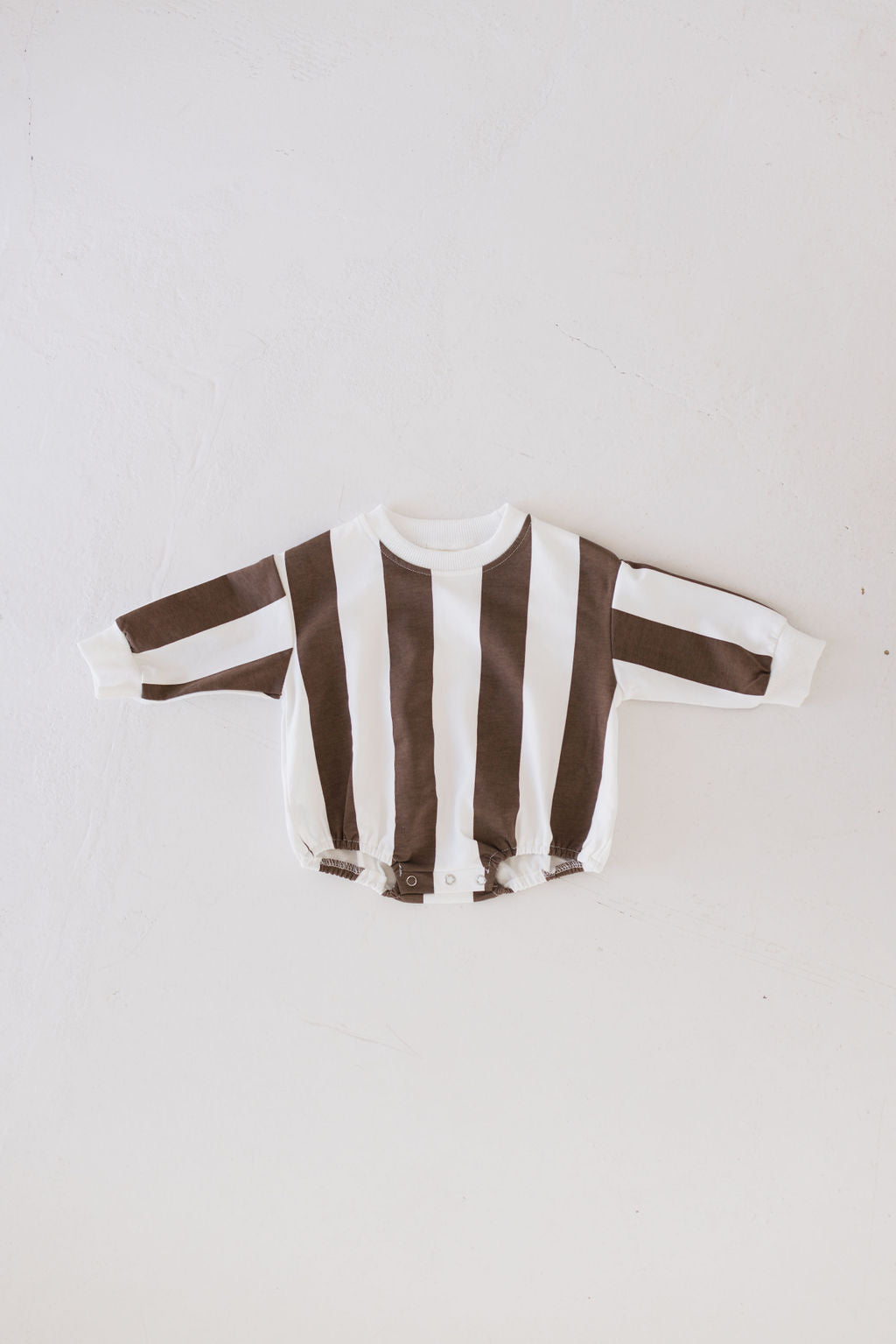 The Sweatshirt Romper | Coffee Shoppe by forever french baby, designed in black and white vertical stripes, lies flat on a white background. It's perfect for creating adorable matching sets with its long sleeves and convenient snap buttons at the bottom for easy changes.