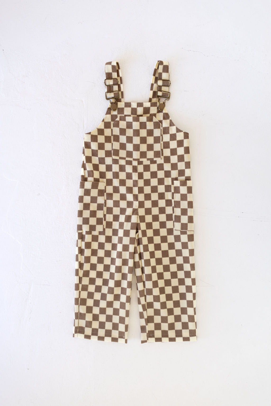 The Honeycomb Checkerboard Corduroy Overalls from forever french baby are designed with adjustable shoulder straps and multiple pockets for practicality. Featuring a soft corduroy material, these overalls provide both comfort and playful style for any little adventurer when laid flat on a textured white surface.