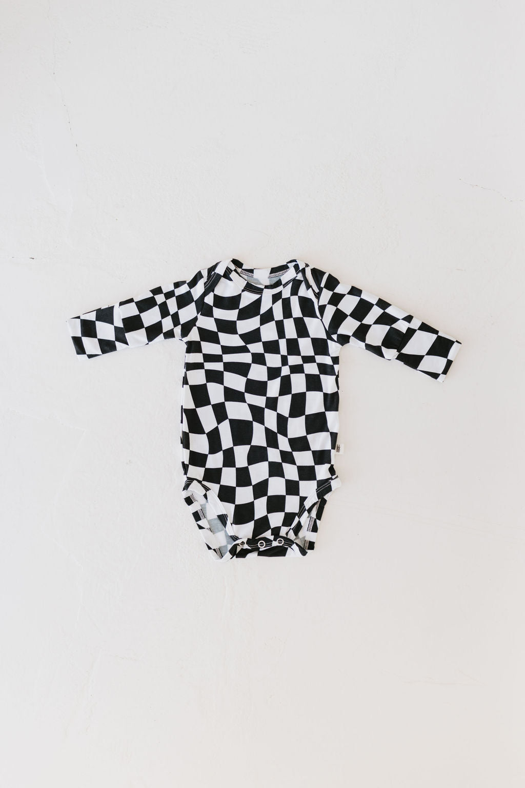 The Long Sleeve Bamboo Snapsuit by forever french baby features a black and white wavy checkerboard design. Made from breathable bamboo fabric, this baby onesie with long sleeves is showcased laid flat on a white background.