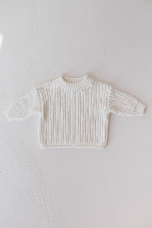 A small, white Knit Sweater | Cloud from forever french baby with a ribbed texture and long sleeves is laid flat against a light-colored surface. This sweater, perfect for your little one's wardrobe, features a crew neckline and simple design, making it suitable for a baby or toddler.