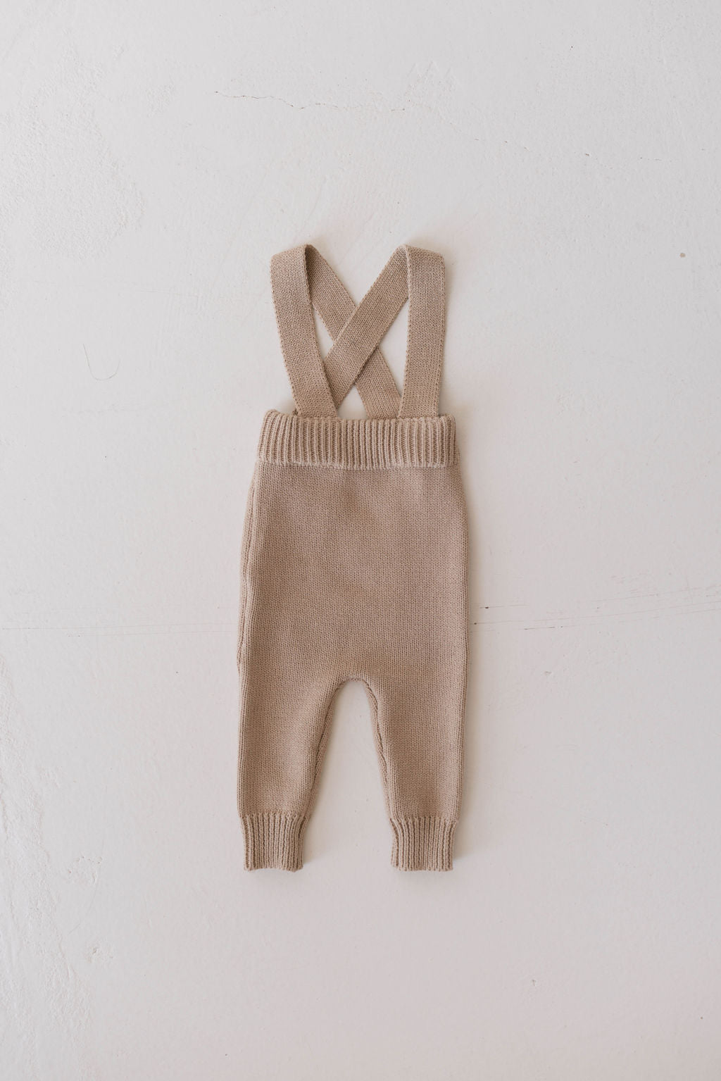 A pair of small, tan-colored Knit Suspenders by Forever French lays flat on a white background. Perfect for cooler weather, the suspenders cross at the back, and the pants, known as Graham, feature ribbed cuffs at the ankles and waistband.