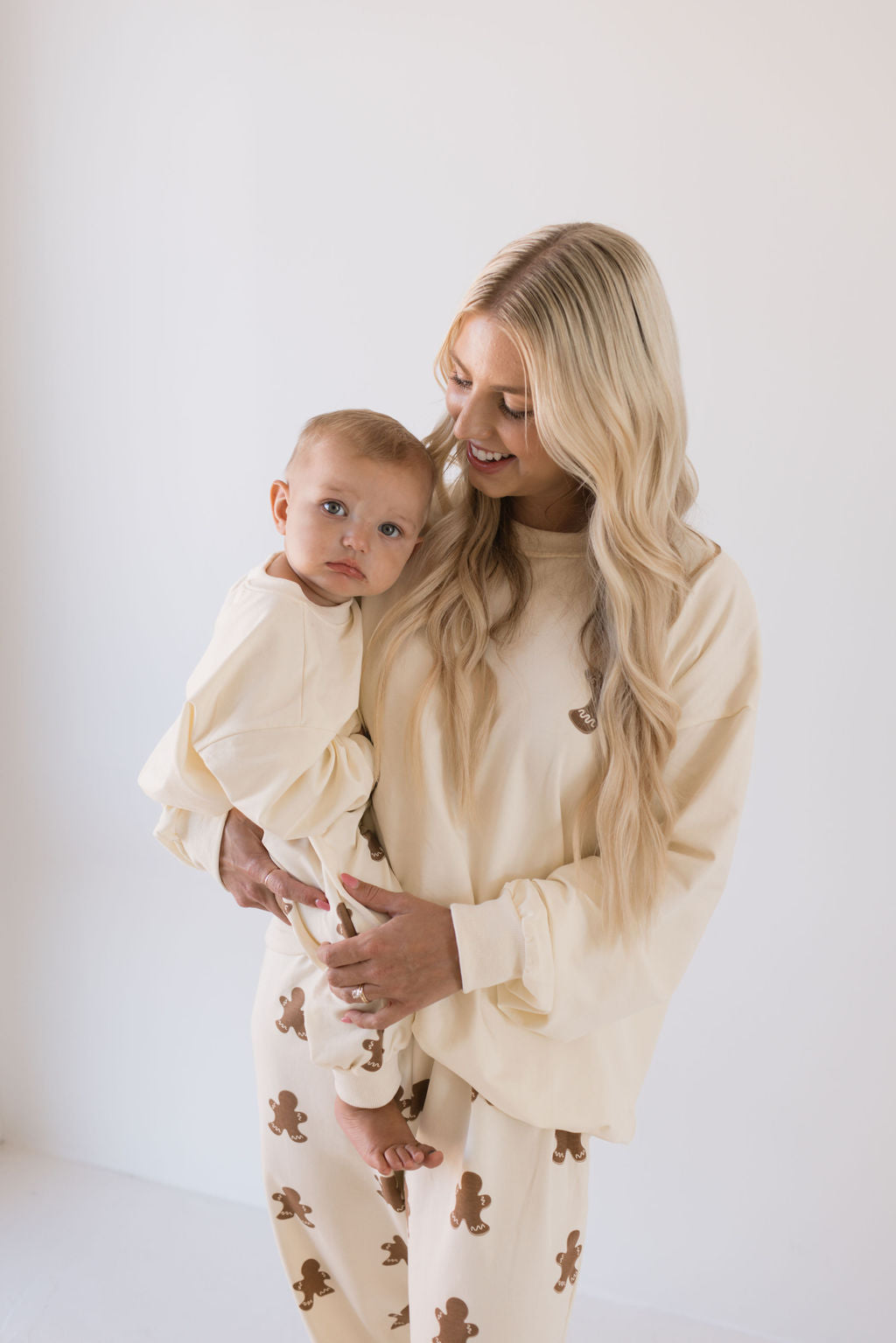 A woman lovingly holds her baby, both adorned in charming matching sweat sets from forever french baby's "Gingerbread" collection, perfectly embodying the holiday spirit.