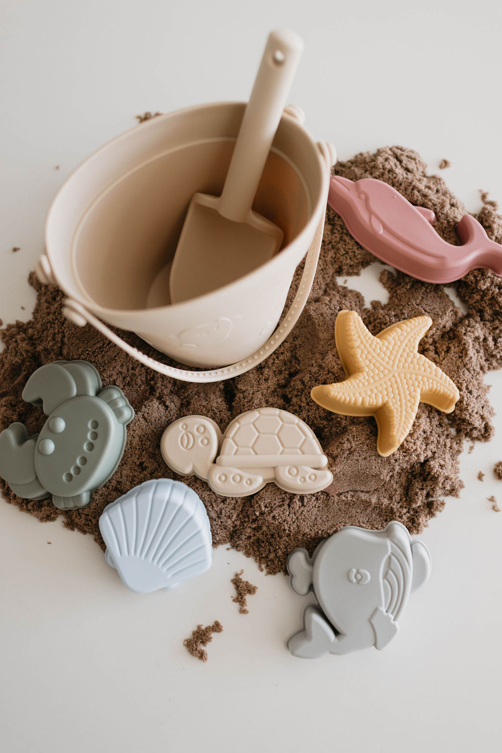 **Product Description:**
The forever french baby Silicone Sand Bucket | 8 Piece set includes a durable silicone sand bucket with a shovel inside, all enveloped by soft, brown sand. Spread around are delightful ocean creature sand molds shaped like a pink crab, yellow starfish, green submarine, beige turtle, blue shell, and gray fish—making it the perfect beach companion for endless fun in the sun.