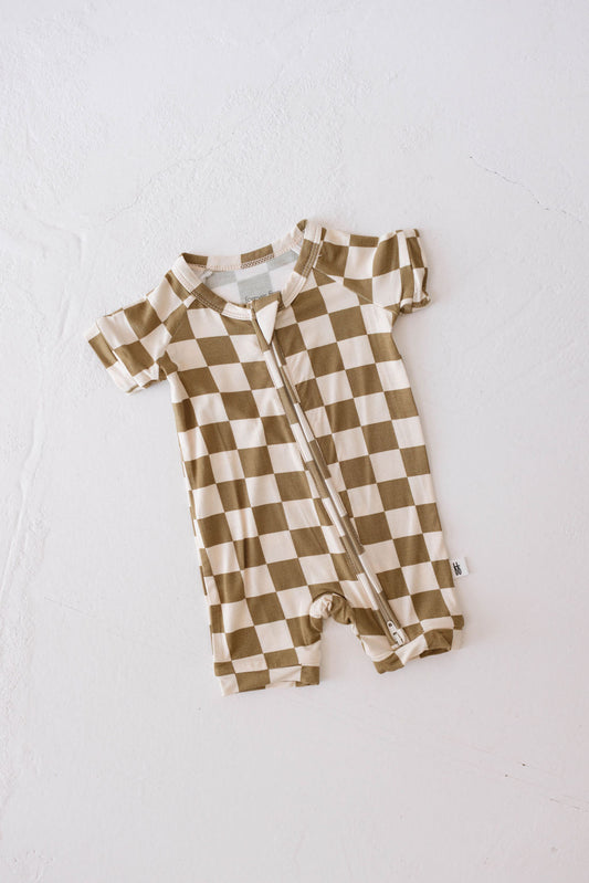 A Shortie Bamboo Zip from forever french baby lies on a white surface. The romper, featuring an Olive Checkerboard pattern in beige and white, is crafted from hypo-allergenic bamboo pajamas fabric and has a front zipper running from the neckline to the left leg opening.