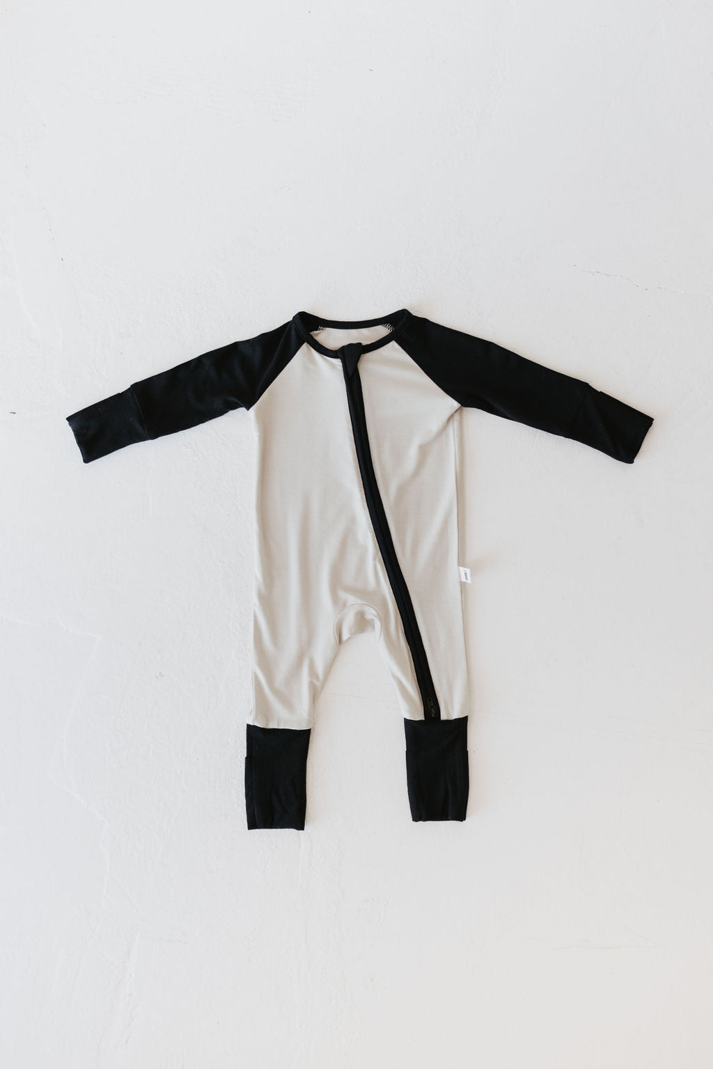 The Bamboo Zip Pajamas from forever french baby, in the Steamboat Willie design, are displayed flat on a white background. This baby onesie features long black sleeves and cuffs that contrast stylishly with its light gray body, and is made from breathable bamboo fabric. A convenient diagonal zipper runs from the neck to the left leg for easy access.