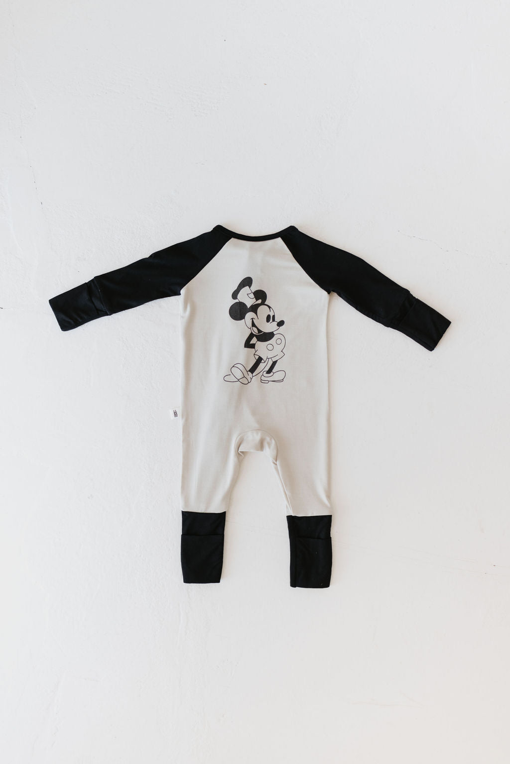 The Bamboo Zip Pajamas | Steamboat Willie by forever french baby features a hypo-allergenic white and black baby romper with long sleeves, made from breathable fabric. It showcases a cartoon mouse character holding a paintbrush and palette on the back, making it ideal for sensitive skin. The romper is displayed flat on a white background.