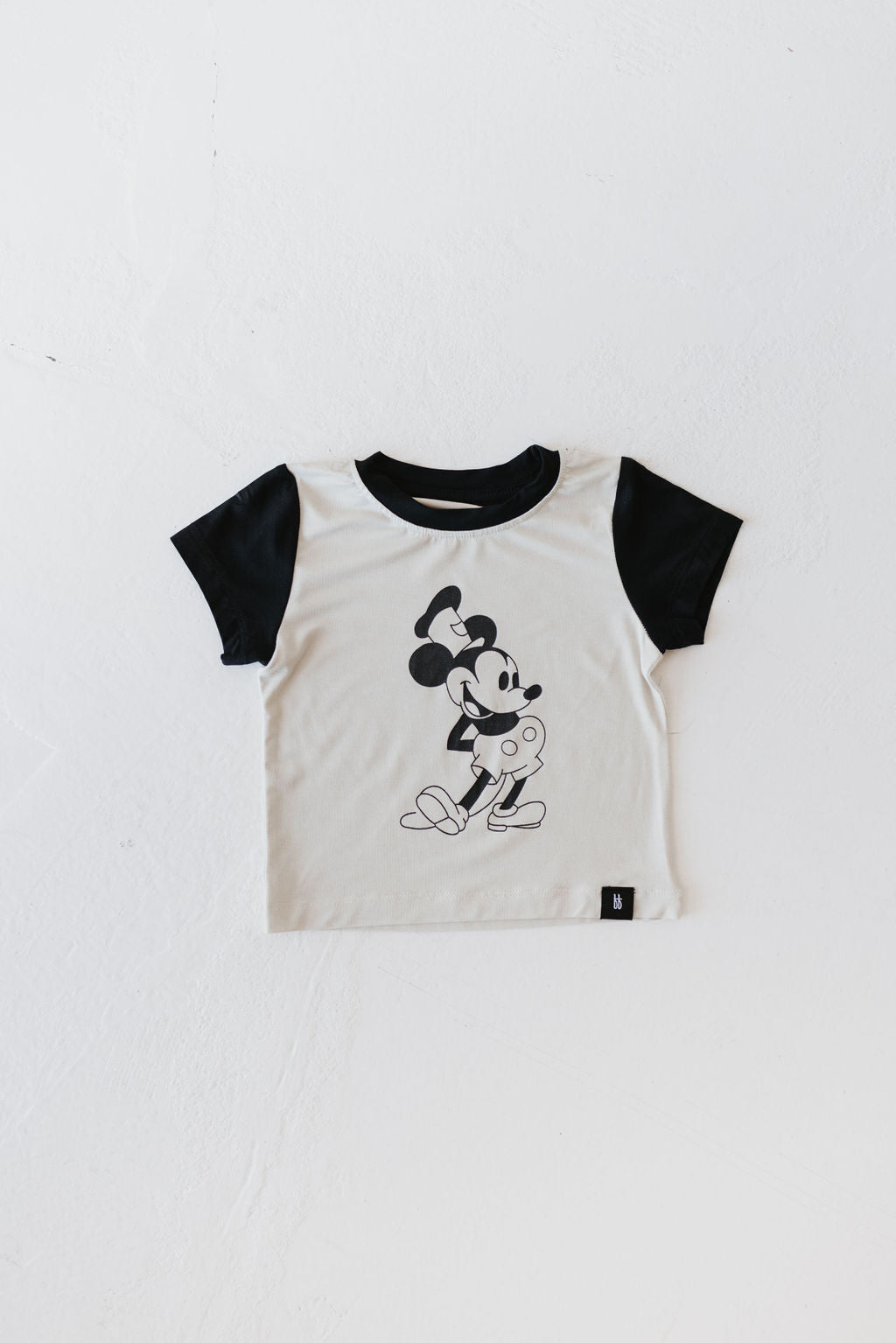 Introducing the "Children's Bamboo Tee | Steamboat Willie" from forever french baby: This charming children's T-shirt features black sleeves and a monochrome cartoon mouse graphic on the front, set against a simple, light-colored backdrop. Made from breathable bamboo fabric, it's ideal for keeping kids comfortable and stylish throughout the day.