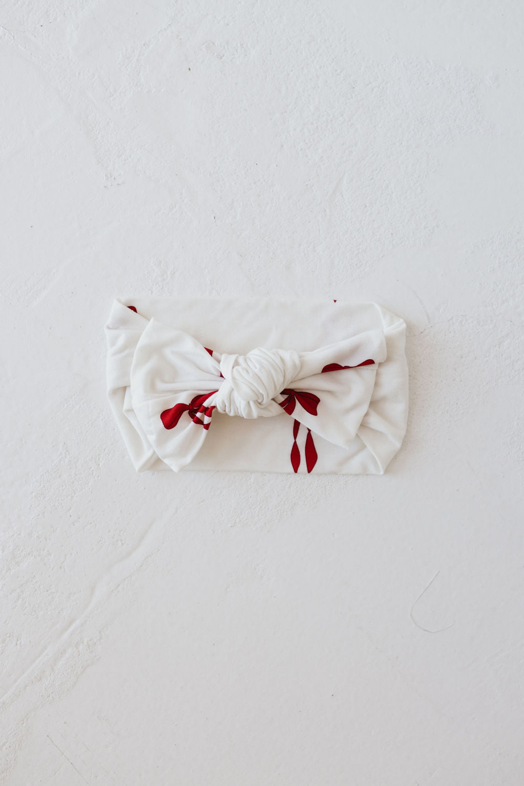 A charming bow from the Bamboo Head Wrap | Ribbons & Bows collection by forever french baby is beautifully displayed on a textured white surface, evoking the look of a delicate bamboo head wrap.