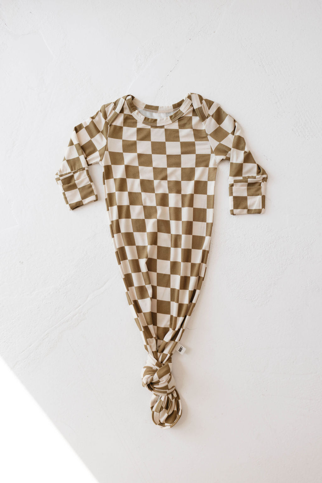 An Olive Checkerboard-patterned newborn gown from Forever French Baby is laid flat against a light background. The hypo-allergenic Bamboo Knotted Gown has long sleeves, a rounded neckline, and a knotted bottom. The fabric appears soft and comfortable.