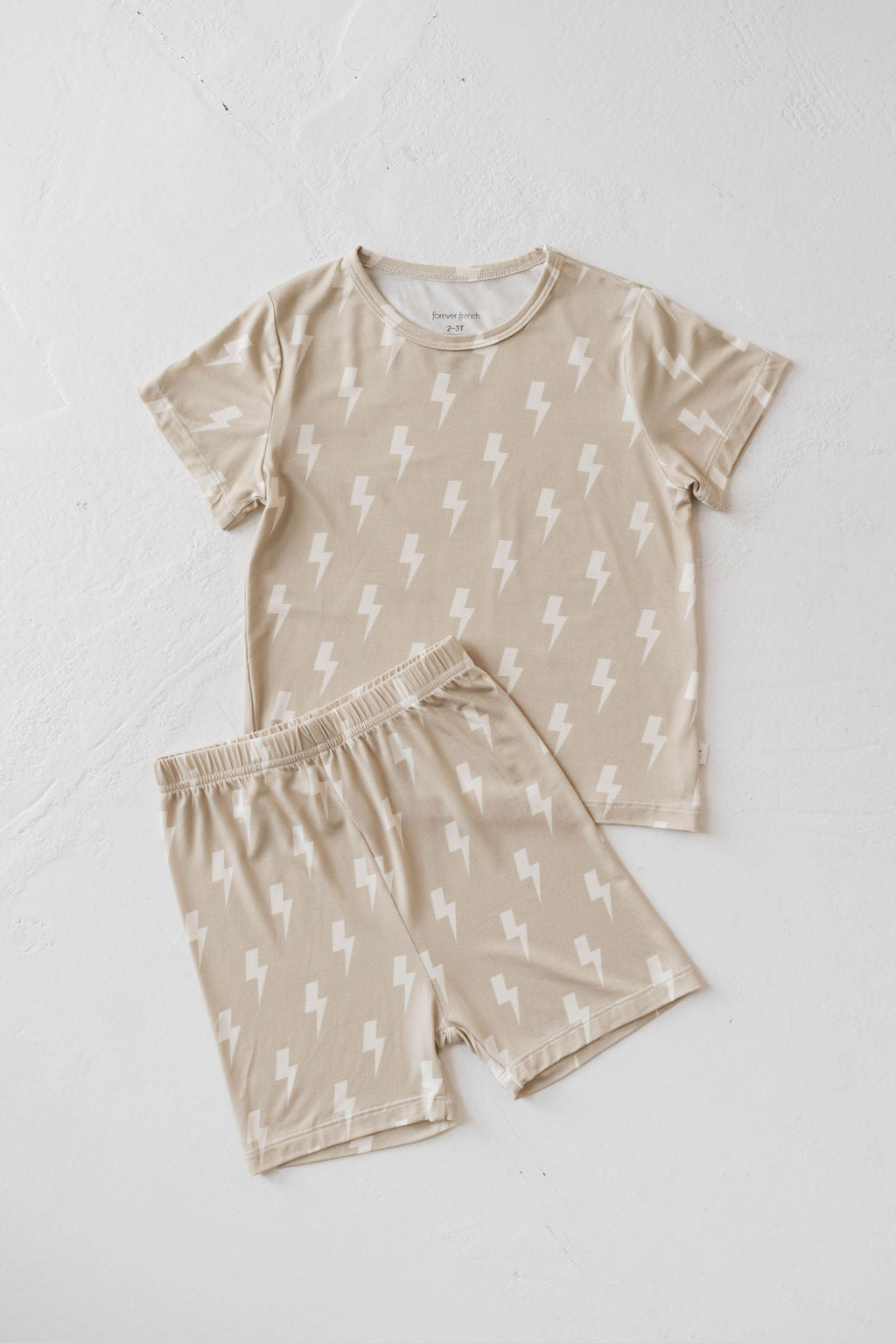 Introducing the Bamboo Short Set | Tan Bolt from forever french baby: a stylish beige children's clothing set featuring a T-shirt and shorts adorned with white lightning bolt patterns, all showcased on a white background. The short-sleeved T-shirt and elastic waistband shorts ensure that your child stays cool and comfortable in this breathable outfit.