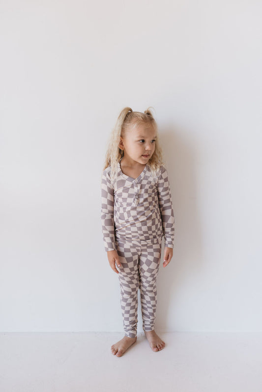 A child stands against a plain white backdrop, dressed in breathable Bamboo Two Piece Pajamas in the Smokey Wave pattern from forever french baby. Her light hair is styled into pigtails as she gazes to the side, exuding comfort and charm.