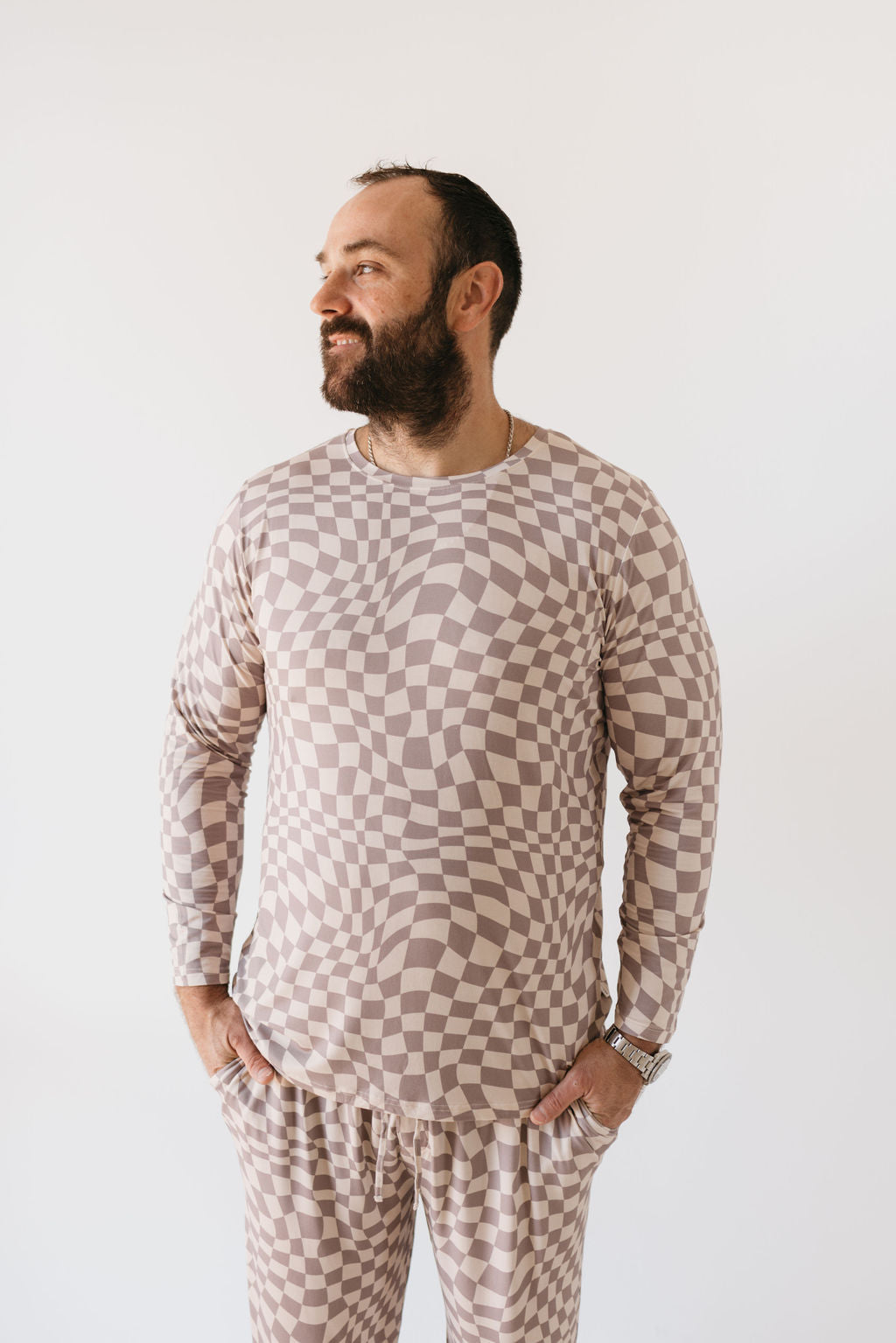 A man with a beard, dressed in the Men's Bamboo Pajamas in Smokey Wave from forever french baby, stands with his hands in his pockets, looking to the side against a plain white background.