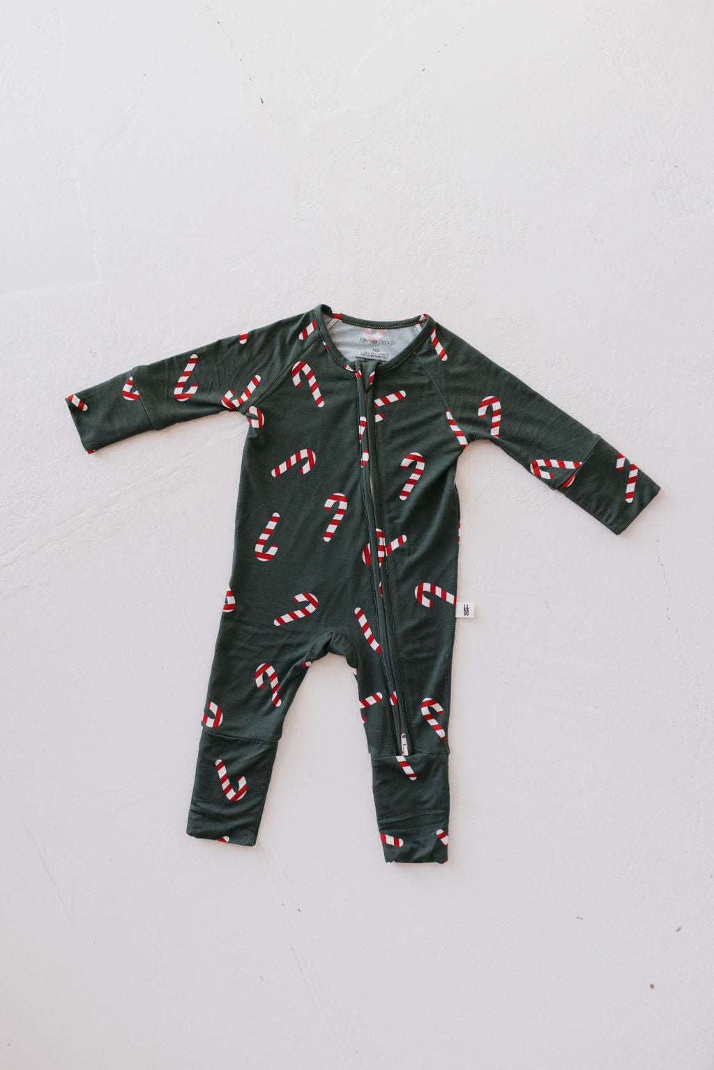 The Bamboo Zip Pajamas | Candy Cane Lane by forever french baby feature a long-sleeved design crafted from breathable bamboo fabric. These pajamas boast a dark green background with a charming pattern of red and white candy canes, plus a convenient zipper for easy dressing. Laid flat on a white surface, these hypo-allergenic pajamas ensure comfort for your little one.