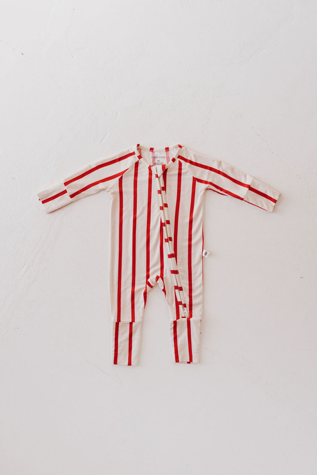 A red and white striped baby onesie from forever french baby, known as the Bamboo Zip Pajamas | the Claus, is displayed on a light surface. The design highlights its long sleeves and legs, with breathable fabric and a convenient diagonal zip front for easy changes.