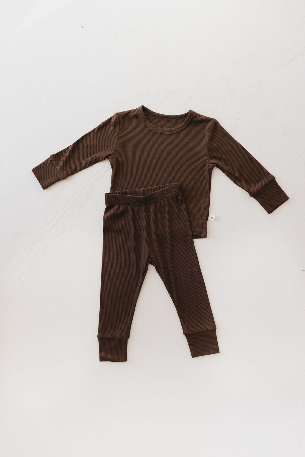 The Bamboo Two Piece Lounge Set in Coffee Bean by forever french baby, a brown long-sleeve pajama set for toddlers with matching pants made from breathable bamboo fabric, is displayed on a light surface.