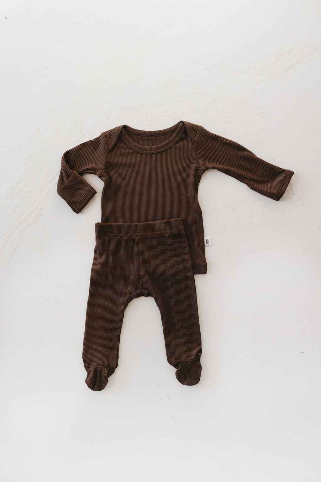 A Sleepy Time Set in the Coffee Bean color from forever french baby is laid out on a light surface. This hypo-allergenic set, made from breathable bamboo, includes a long-sleeve top and matching footed pants designed with infants' comfort in mind.