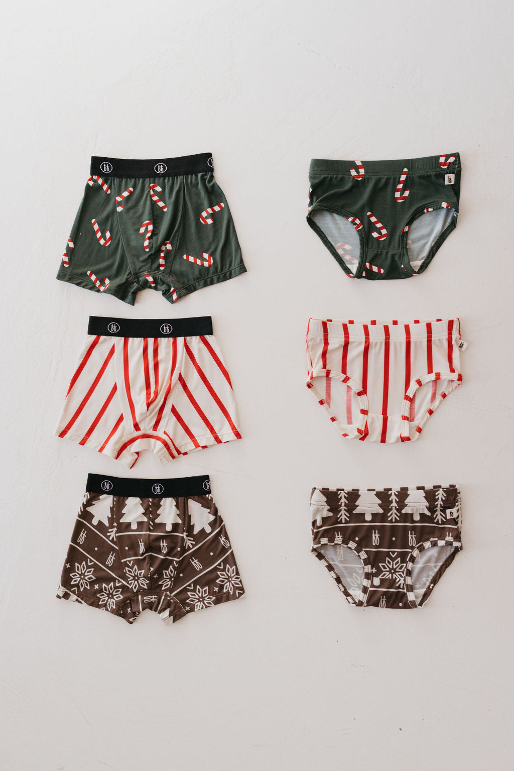 Six pairs of Bamboo Boxers from the "Bamboo Boxers (3 Pack) | 'tis the Season" collection by forever french baby feature holiday-themed designs crafted from super soft fabric. The pairs are arranged in two columns and showcase patterns like green with candy canes, red and white stripes, and brown with snowflakes and trees. Each pair ensures comfort with a flexible elastic band that provides a perfect fit.