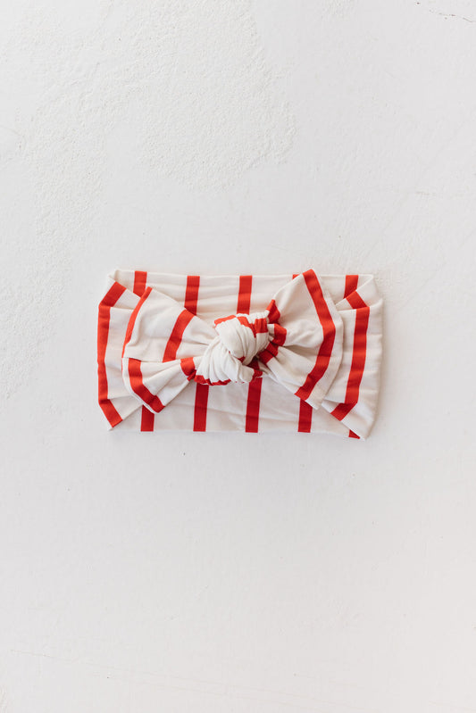 Set against a plain white background, the Bamboo Head Wrap | the Claus by forever french baby features a prominent knot at the center. This stylish headband has red vertical stripes on white and is adjustable, making it an ideal accessory for babies and toddlers.