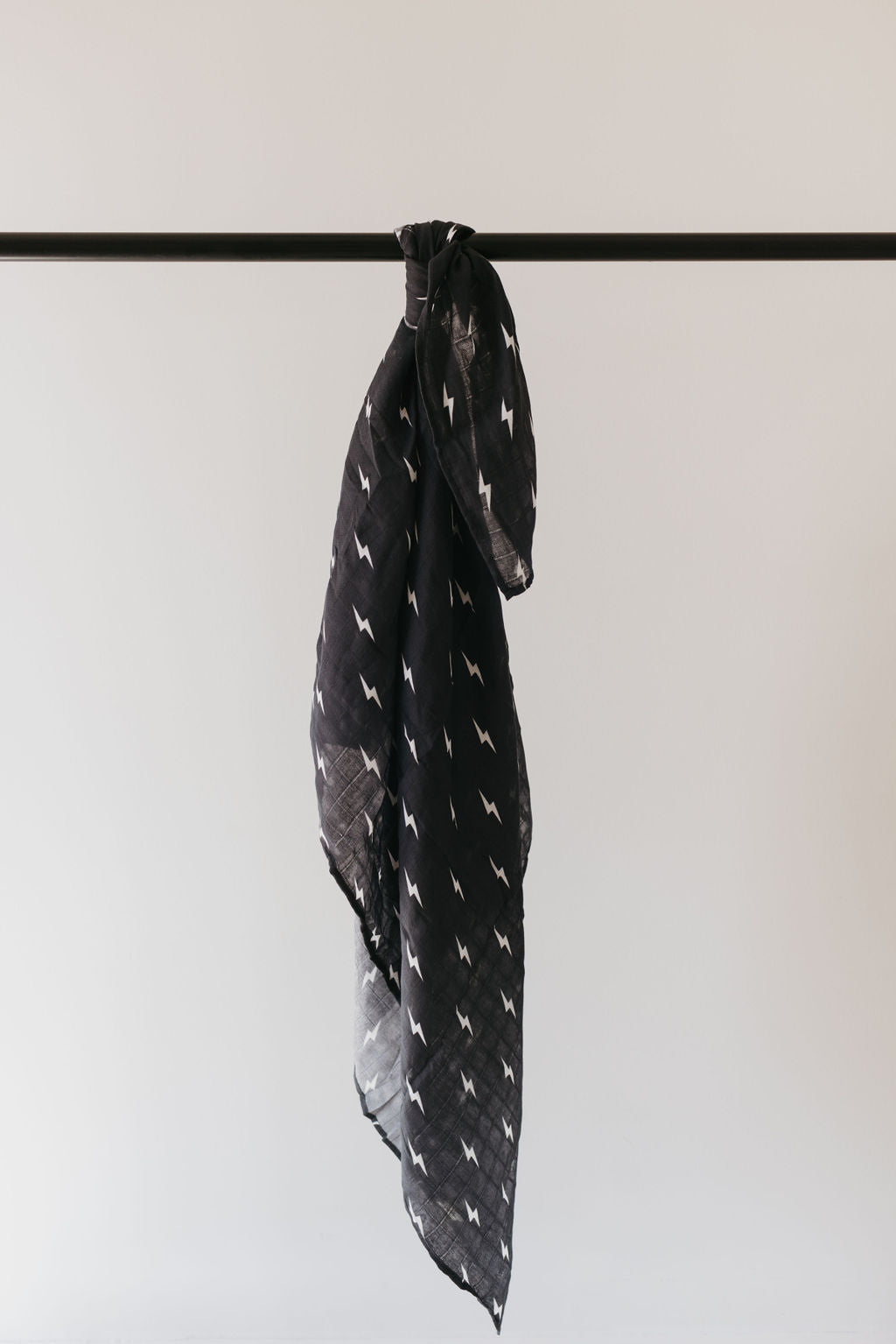 A midnight lightning bolt muslin swaddle from Forever French Baby hangs from a horizontal rod against a plain light gray background.